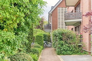 A narrow pathway leading to a brick building with a balcony.