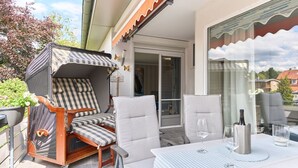 Une terrasse dotée d’un espace salon couvert, d’une table avec des verres et d’une vue sur la rue.