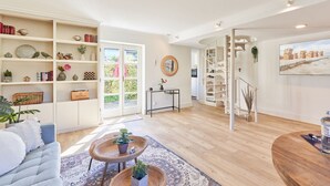 En rummelig stue med et stort bogreol, en behagelig sofa, et lille rundt bord med planter, og en trappe til en etage ovenpå.