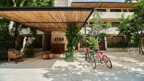 Un espace extérieur abrité, aménagé avec des sièges, comprenant une chaise en osier et un vélo rouge.