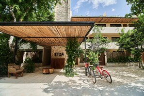 Relax in the shaded outdoor seating area under a pergola, surrounded by lush greenery and the ITZA building's stone facade.