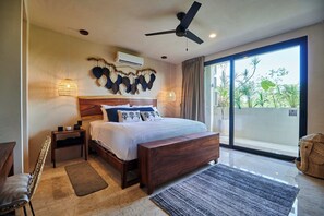 Relax in this serene bedroom with a large bed, wooden bench, and sliding glass door leading to a lush outdoor space.