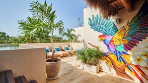 Une terrasse sur le toit dotée d’une piscine, de chaises longues et d’une fresque représentant un oiseau aux couleurs vives.