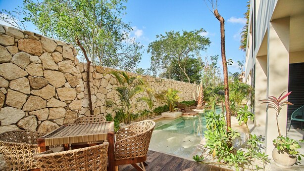 Un mur de pierre, des sièges en plein air, une piscine et des plantes tropicales.