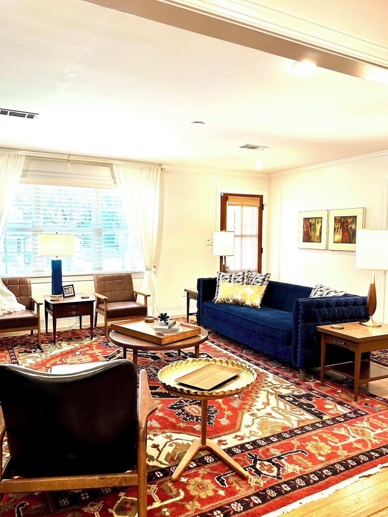 Un salon avec un canapé bleu, une table basse en bois, un tapis à motifs et une fenêtre avec des rideaux.