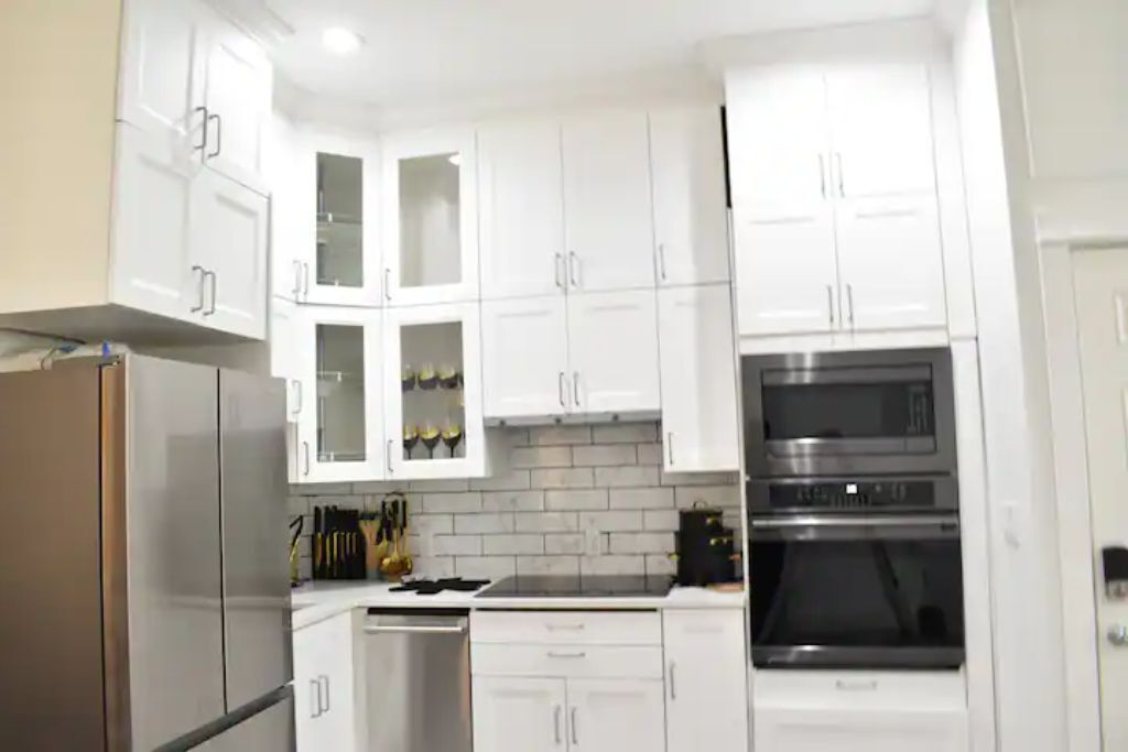 A modern kitchen with white cabinets, a stainless steel refrigerator, a dishwasher, and a built-in oven.