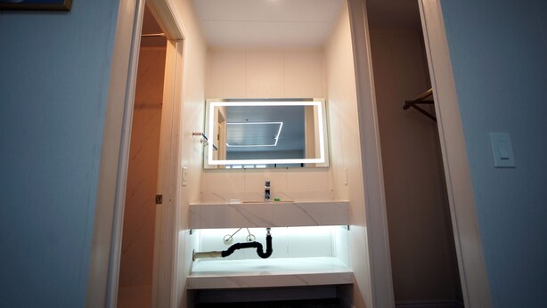 A bathroom with a white sink, a mirror with a lighted frame, and a towel rack. - Airport Stay Motel (Ontario)