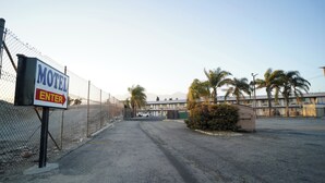 A motel entrance with a chain-link fence, palm trees, and a building in the background. - Airport Stay Motel (Ontario)