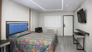 A modern hotel room with a bed, a desk, a chair, a TV, and a door. - Airport Stay Motel (Ontario)