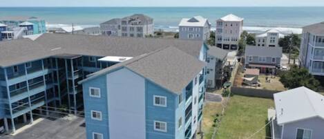 A coastal residential area with multi-story buildings, a parking lot, and a view of the ocean.