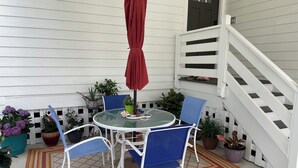 Un patio con una mesa redonda, dos sillas azules, un paraguas rojo y plantas en macetas.