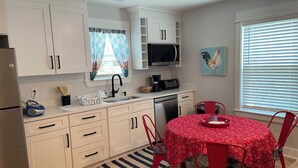 Una cocina moderna con armarios blancos, microondas, fregadero y comedor con una mesa y sillas rojas.