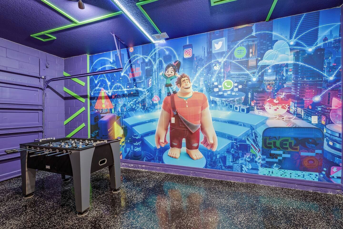 A room with a foosball table, a mural with social media icons, and a cityscape design on the wall.