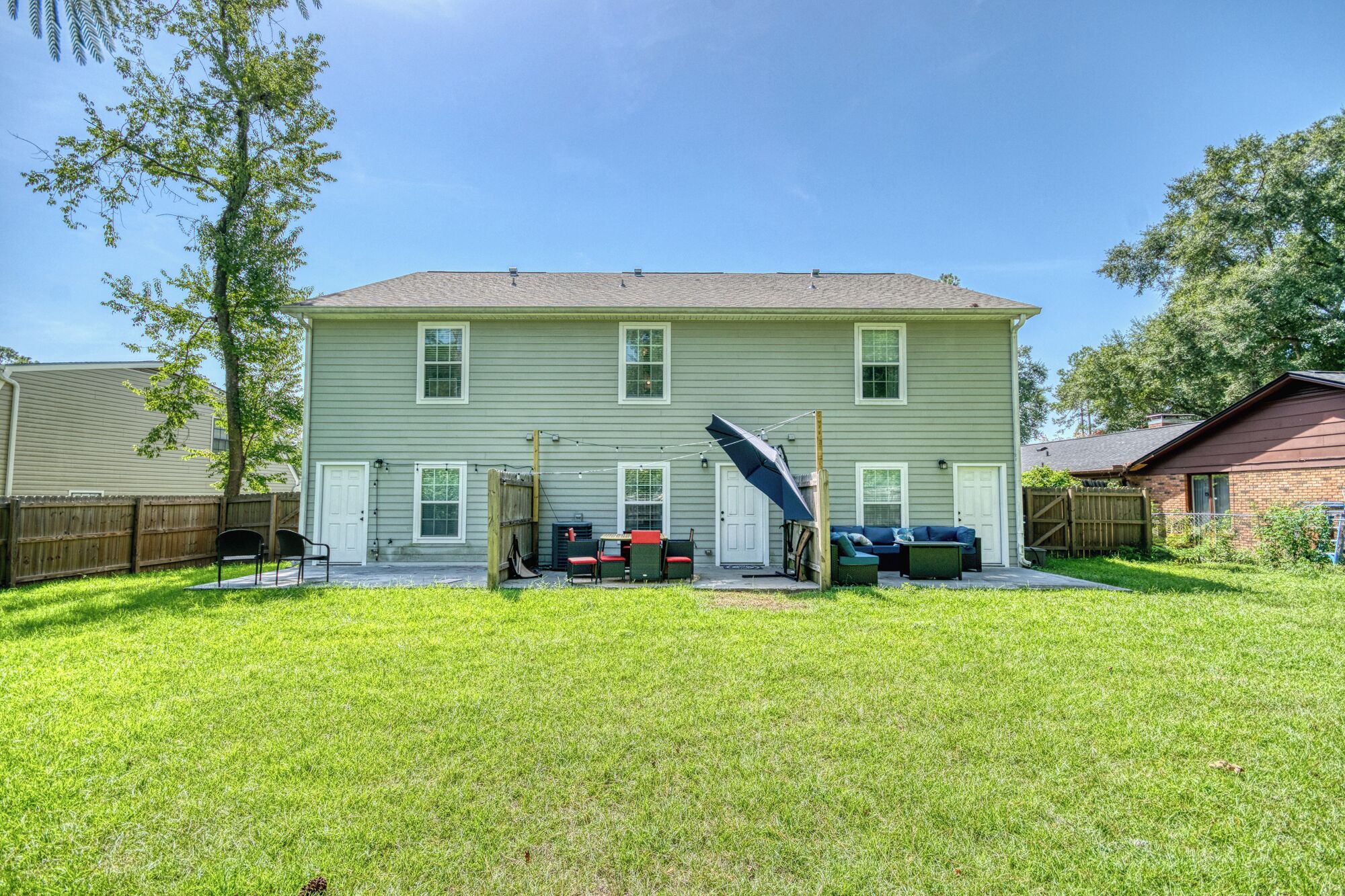 A two-story house with a front yard, a patio with outdoor furniture, and a backyard with a fence.
