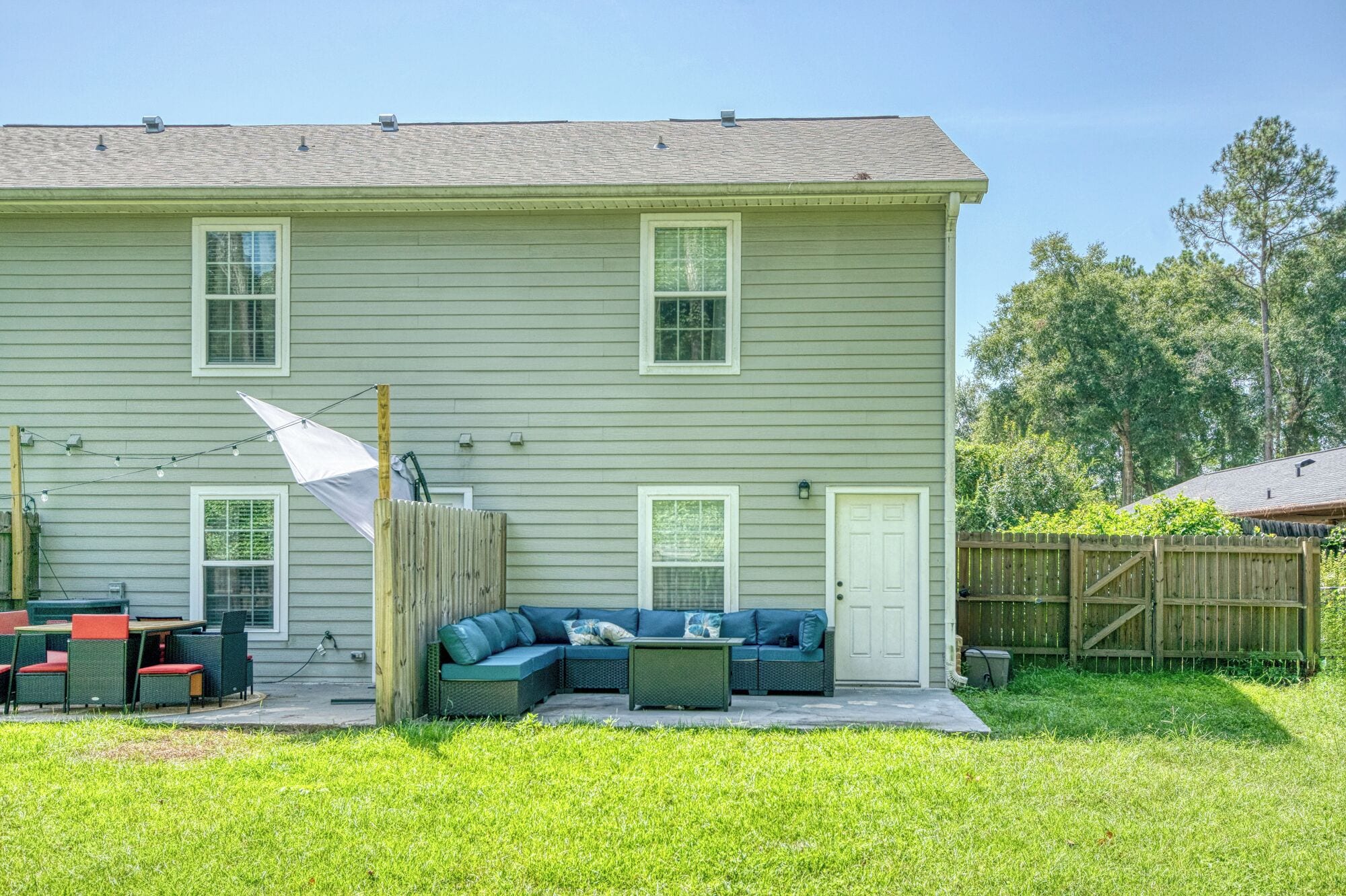 A two-story house with a green exterior, a covered patio area with outdoor furniture, and a wooden fence.