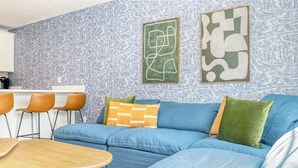 Una sala de estar moderna con un sofá azul, una mesa de centro de madera y una pared con estampado.