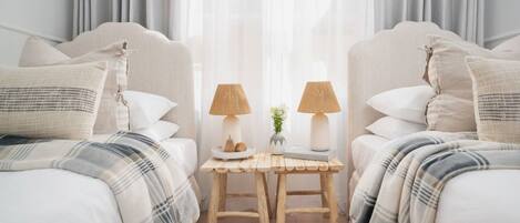 Un dormitorio con dos camas, cada una con cabecero, una mesita de noche con lámpara y un pequeño jarrón con flores.