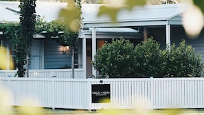 A building with a white fence, a sign reading 'HAUS + HEIM ACCOMMODATION', and a covered porch area.