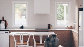 A kitchen with white cabinets, a white countertop, and two windows. There are two white chairs and a table with two metal pitchers on it.