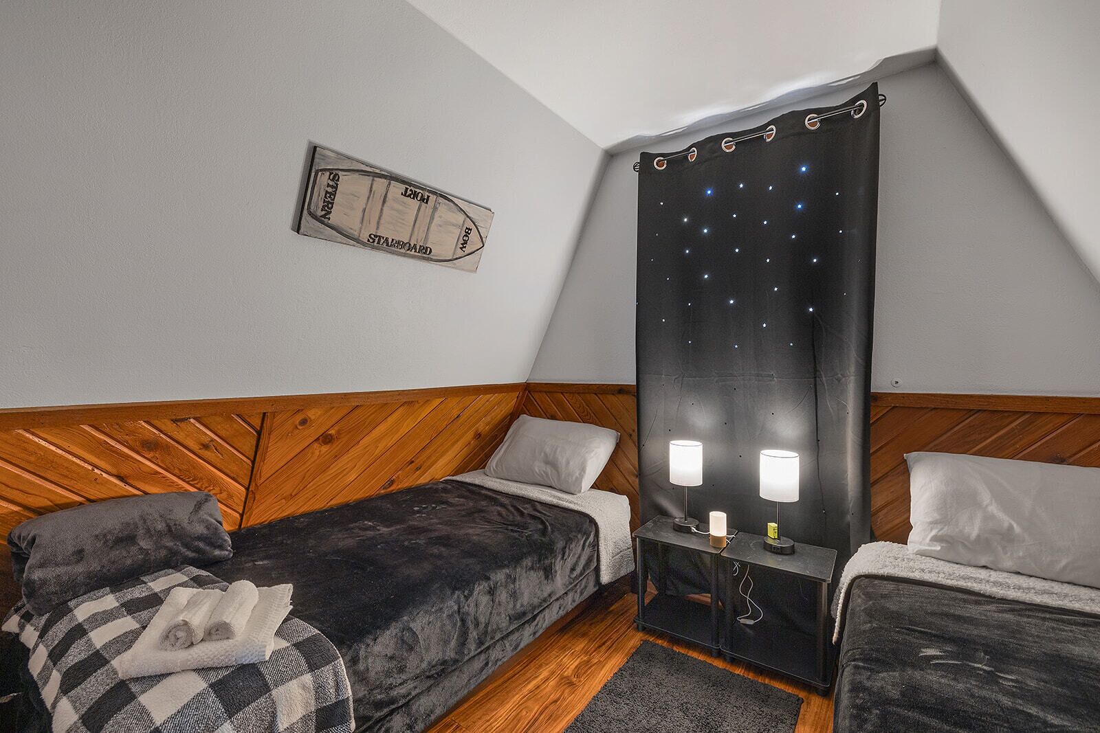Quarto com duas camas de solteiro, cabeceira de madeira, mesa de cabeceira com duas luminárias e uma placa indicando estibordo na parede.