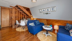 L’intérieur d’un chalet accueillant, avec un escalier en bois, un coin repas et un salon doté d’un canapé bleu et d’une petite table ronde.
