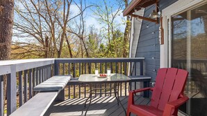Une terrasse en bois avec une table en verre et une chaise rouge, donnant sur une zone boisée.