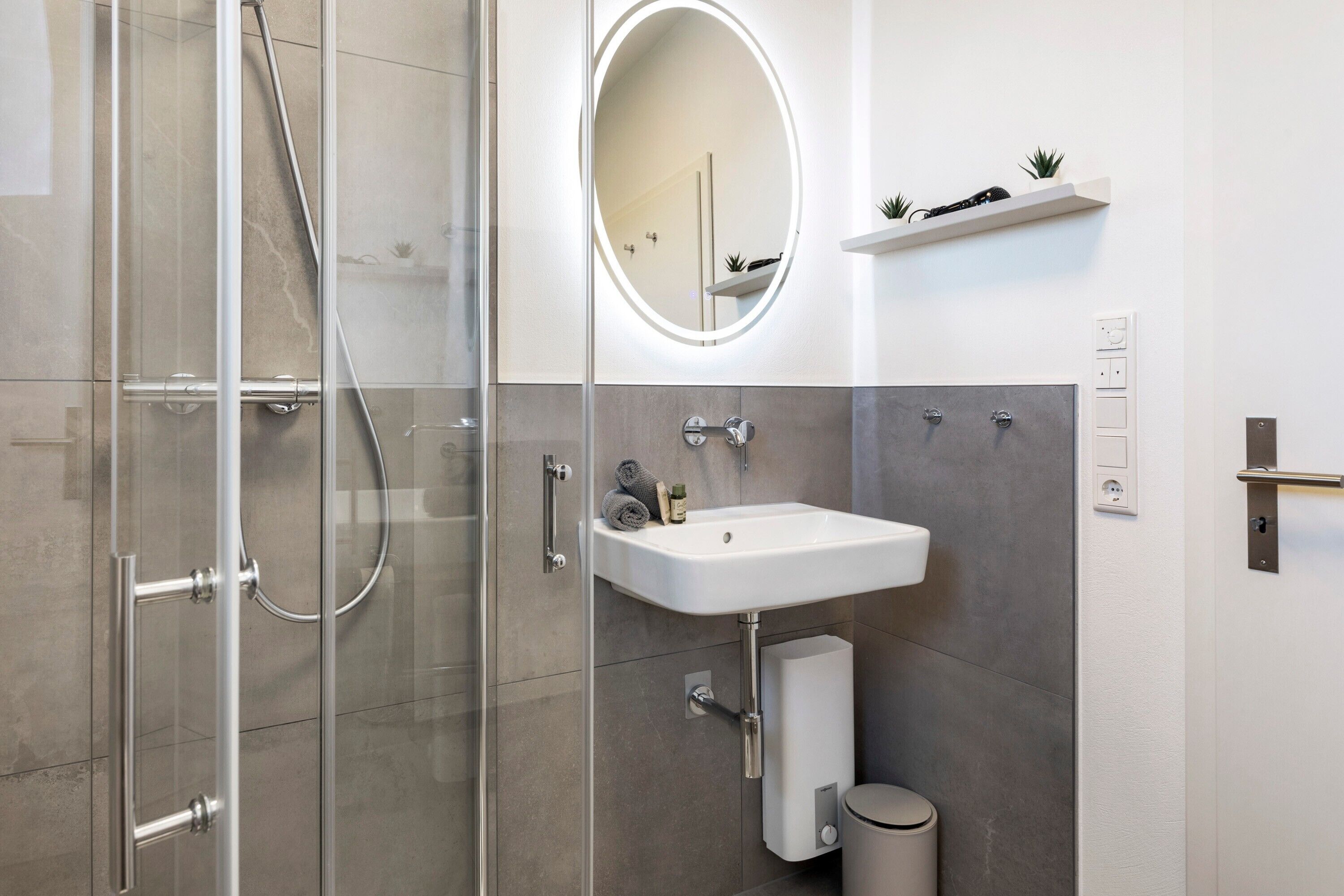 A modern bathroom with a glass shower enclosure, a white sink, and a mirror with a light.