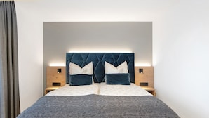 Un letto rifatto con un poggiatesta, due comodini e una tenda a sinistra.