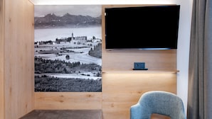 Una stanza con una grande TV a schermo piatto montata su una parete in legno, un tavolino con un telecomando, una poltrona rivestita in blu e una panca.