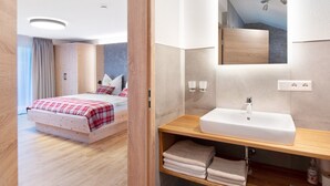 A modern hotel room with a wooden bed, a large mirror above a white sink, and a wooden wardrobe. - Ferienwohnung Rothirsch, 45 qm, 1 Schlafzimmer, 1 Schlafsofa, max. 4 Personen (Höchenschwand)