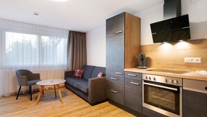 A modern kitchen with a built-in oven, a dining area with a round table and two chairs, and a sofa with a plaid cushion. - Ferienwohnung Rothirsch, 45 qm, 1 Schlafzimmer, 1 Schlafsofa, max. 4 Personen (Höchenschwand)
