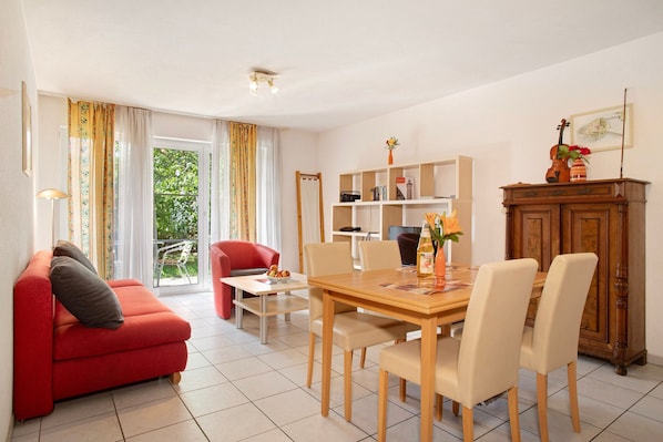 A dining area with a wooden table, chairs, a red sofa, and a bookshelf.