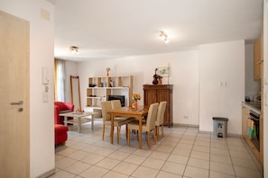 A modern kitchen with a dining area, a red chair, a wooden table, and a small trash bin.