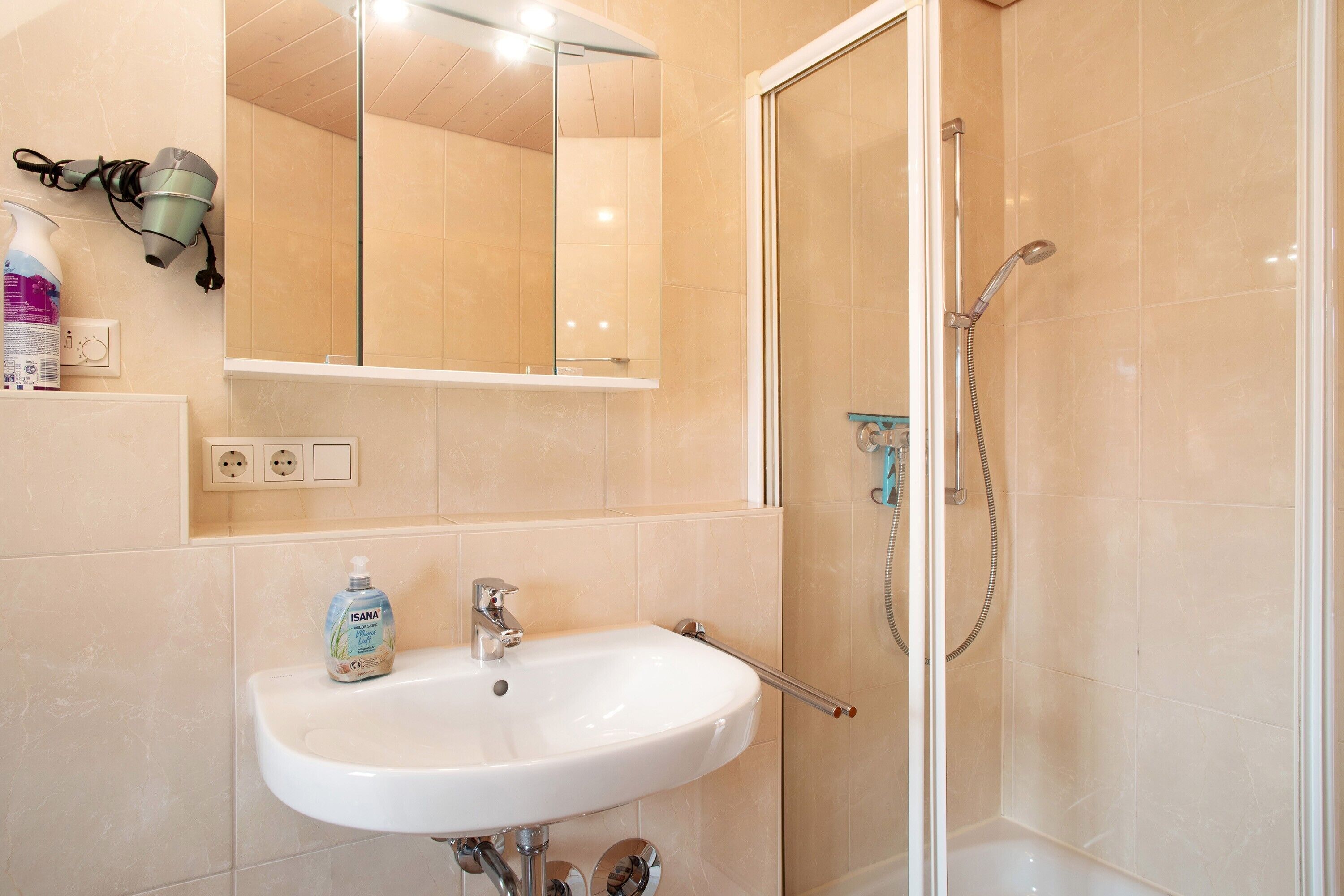 A bathroom with a sink, mirror, hairdryer, and shower.