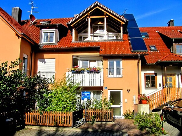 Ein zweistöckiges Gebäude mit Balkon, Holzzaun und einem geparkten Auto davor.