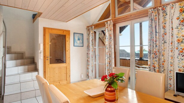 A dining area with a wooden table, chairs, a vase with flowers, and a television. - Maisonette Aparment 3, 75 qm, 2 bedrooms, max. 5 people (Lindau am Bodensee)