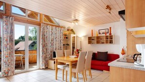 A spacious room with a wooden dining table, chairs, a red sofa, and a kitchen area. - Maisonette Aparment 3, 75 qm, 2 bedrooms, max. 5 people (Lindau am Bodensee)