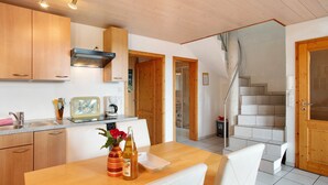 A kitchen with wooden cabinets, a dining table with chairs, a bottle of wine, and a vase with flowers. There is a staircase leading to another level. - Maisonette Aparment 3, 75 qm, 2 bedrooms, max. 5 people (Lindau am Bodensee)
