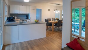 Una cocina moderna con armarios blancos, una zona de comedor con mesa y sillas de madera, y vistas a una terraza exterior.