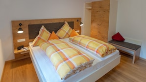 Una cama con ropa de cama escocesa, una mesita de noche con lámpara y un banco con un cojín rojo.