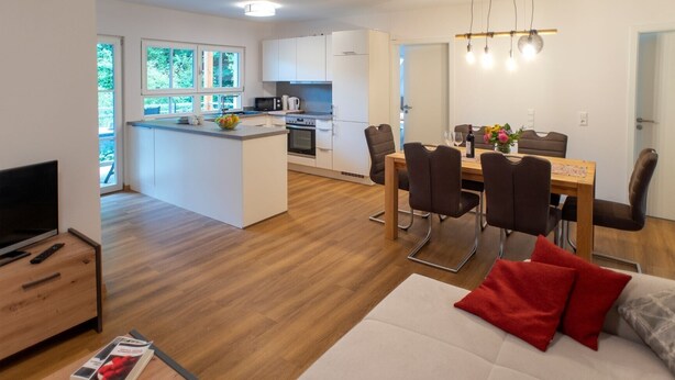 Una sala moderna con un sofá, una mesa de comedor y una cocina con armarios blancos y un microondas.