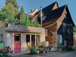 Ein zweistöckiges Gebäude mit roter Tür, einem mit Pflanzen bepflanzten Balkon und einem Schornstein.