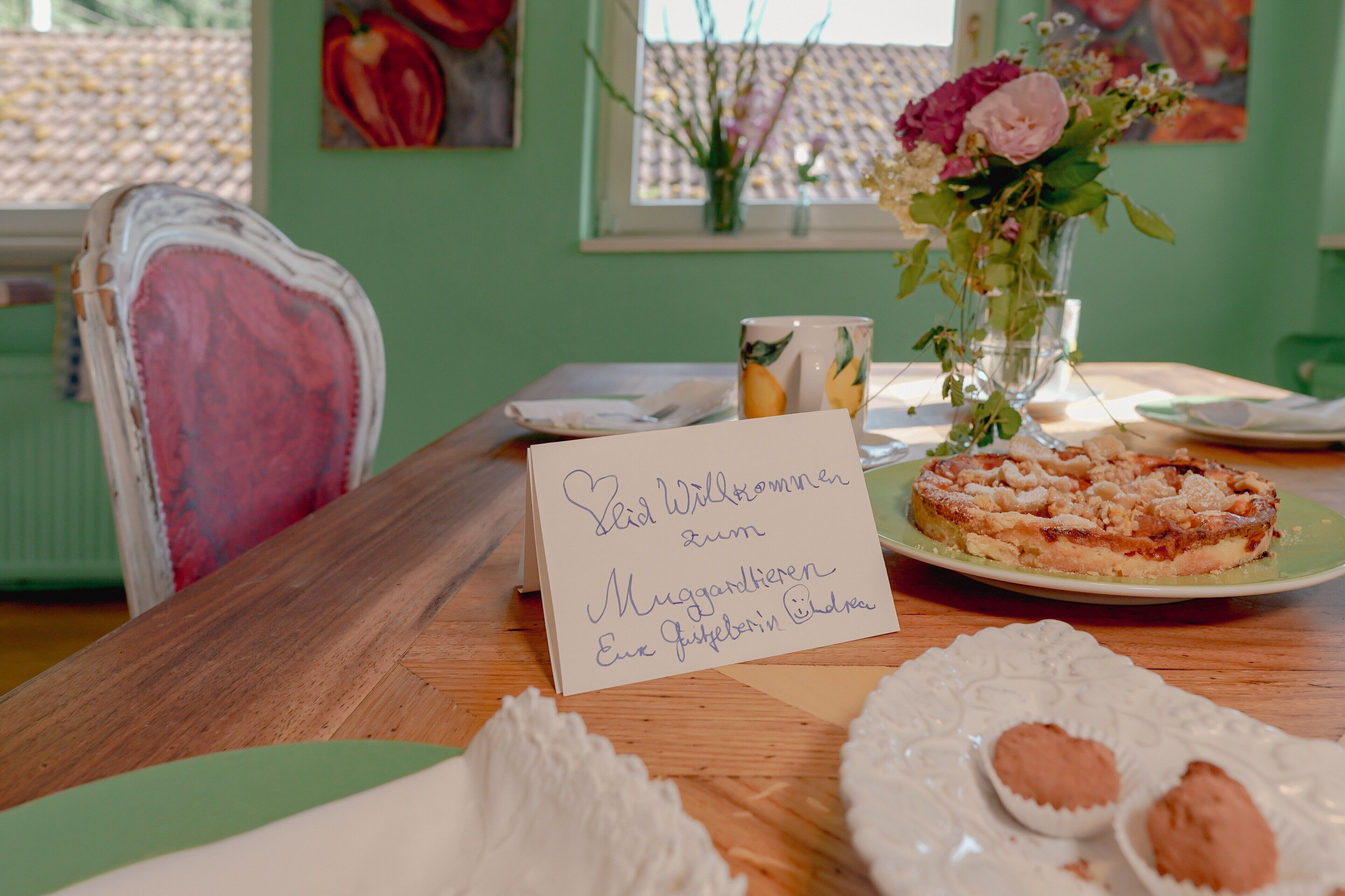 A wooden table with a cake, a card, and a vase of flowers.