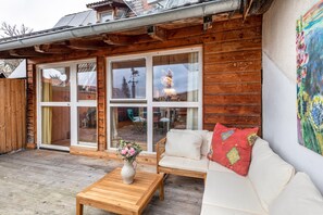 A wooden cabin with a sliding glass door, a wooden deck, a white sofa, and a vase with flowers. - Apartment 'Haus der Malerin Wolke Zwei' with Mountain View, Shared Terrace and Wi-Fi (Müllheim)