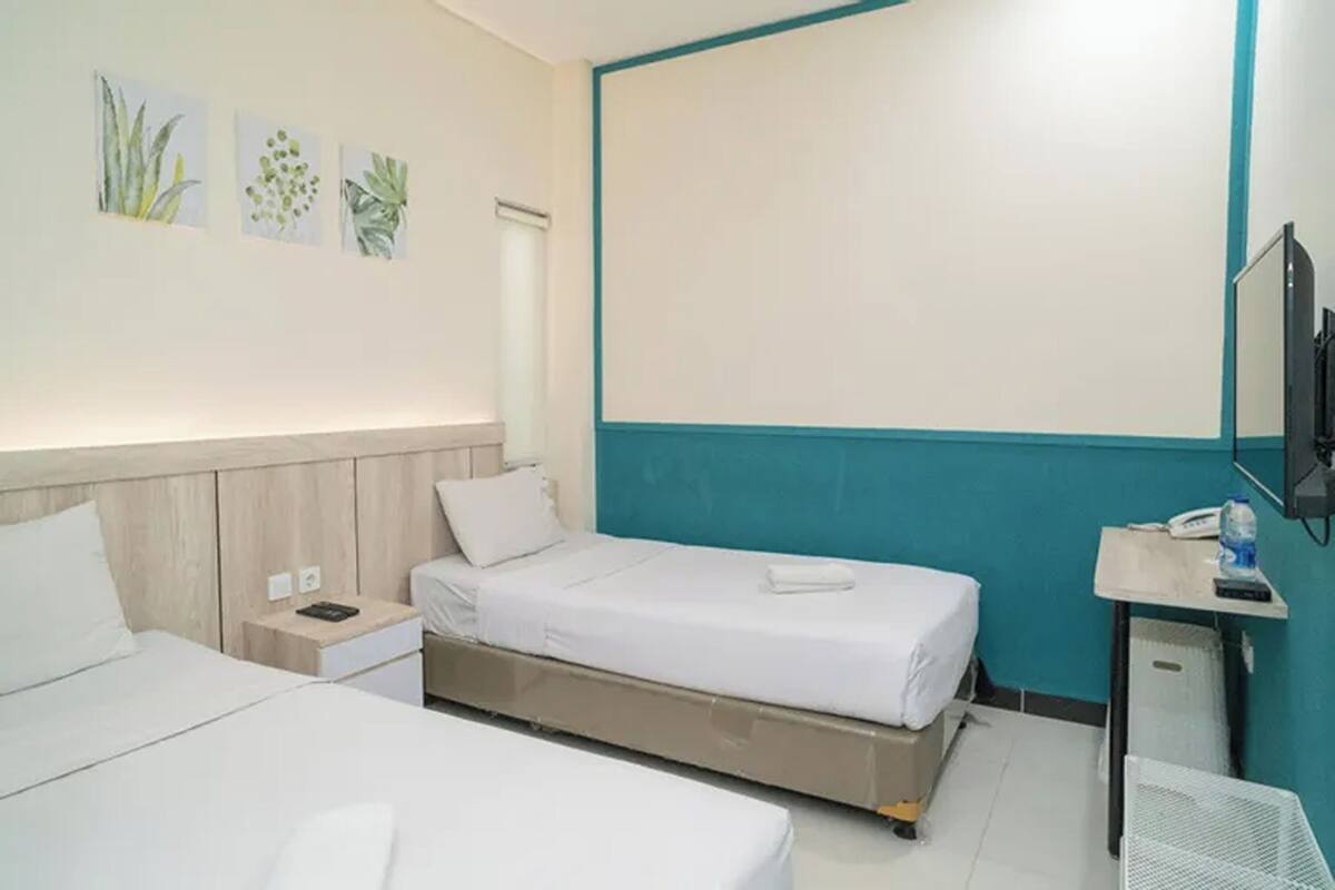A hotel room with two beds, a desk, a TV, and wall art.