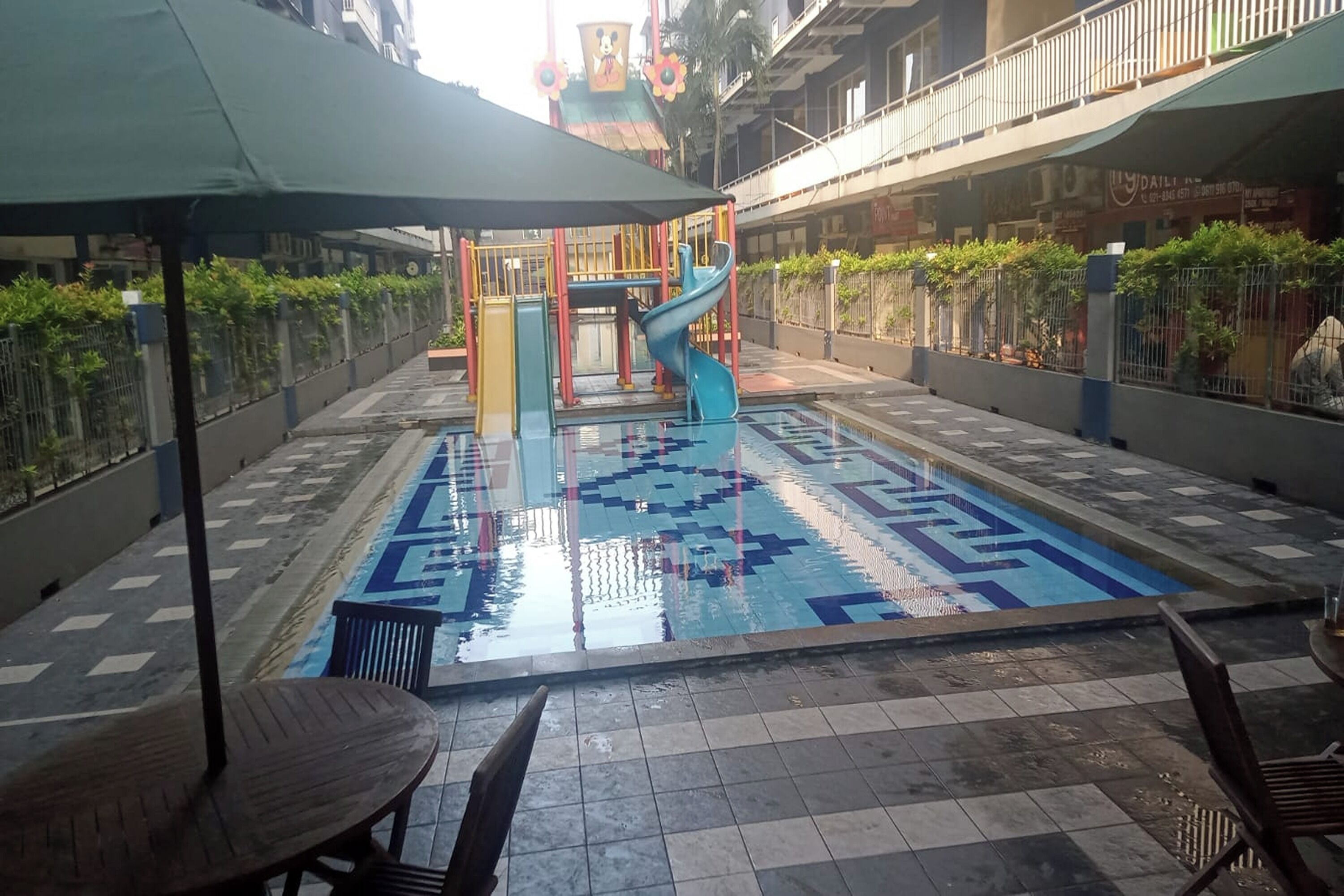 A courtyard with a children's play area, a swimming pool, and seating arrangements.