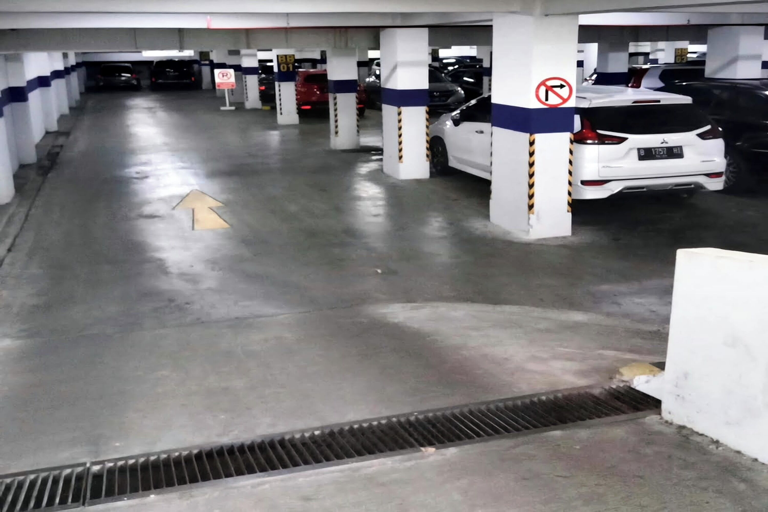 A multi-level parking garage with cars parked in designated spaces, concrete pillars, and directional arrows on the floor.