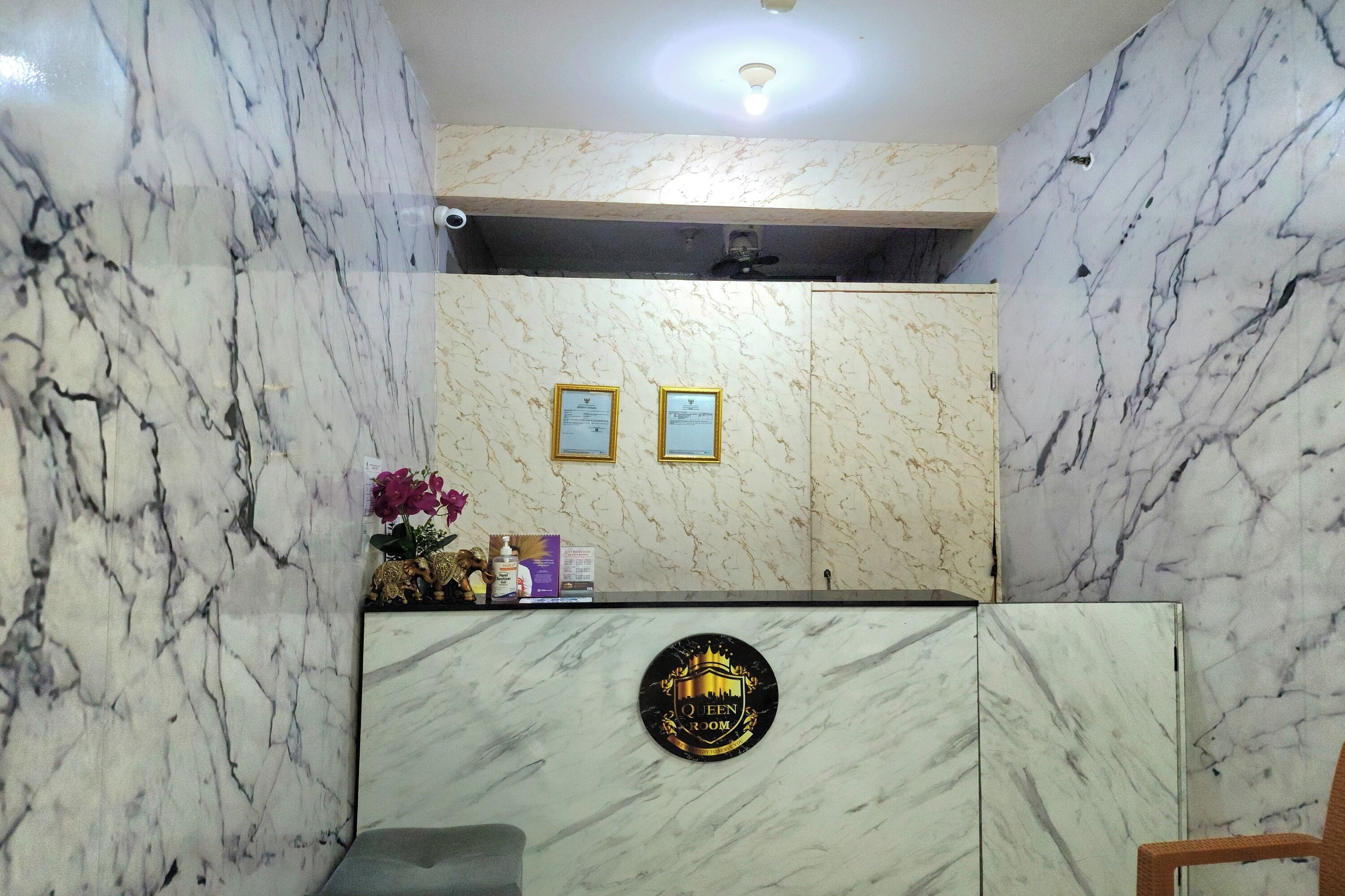 Una recepción con pared de mármol, certificados enmarcados y un cartel que indica 'Queen Room'.