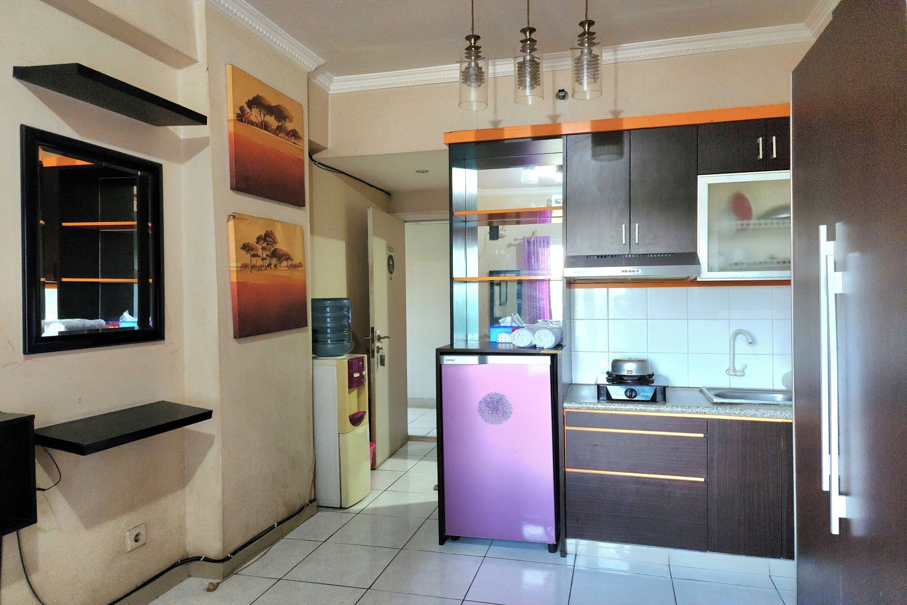 A compact kitchen with a refrigerator, a water dispenser, and a microwave. There are cabinets, a sink, and a window above the sink.