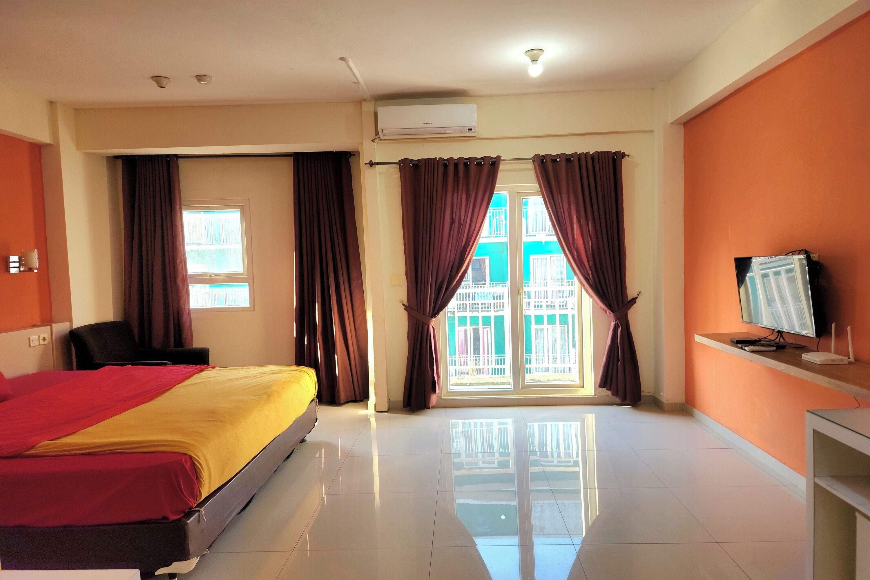Habitación de hotel con una cama, un escritorio con computadora, aire acondicionado y una ventana con cortinas.
